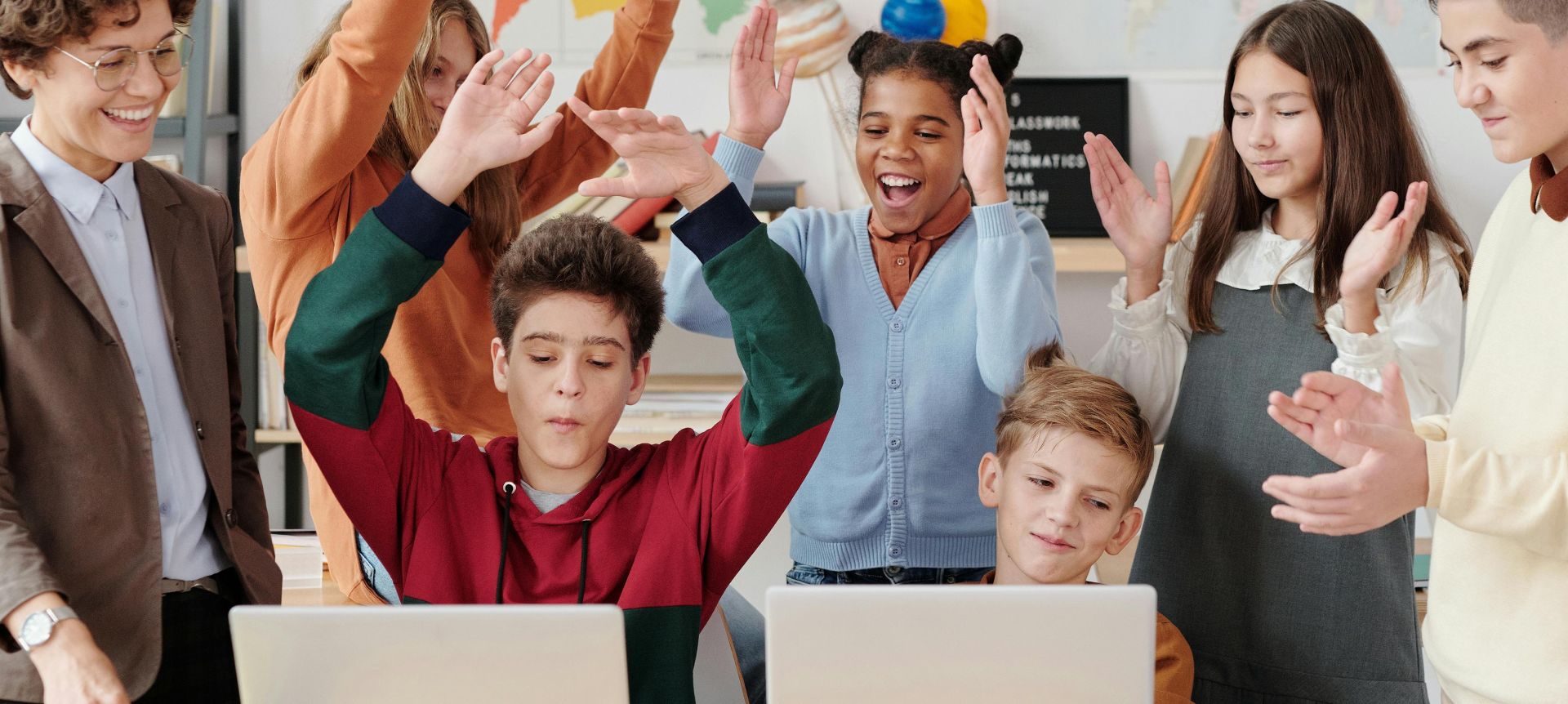 A group of happy students and a teacher clapping together in a school classroom.